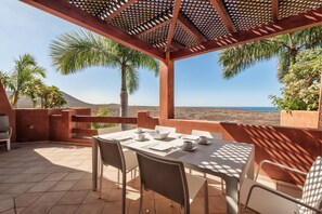 An outdoor dining area with a table set for two, overlooking a desert landscape and the sea. - Bahia - Alzaro 1.3 DELUXE SEA VIEW & JACUZZI 3B (Arona)
