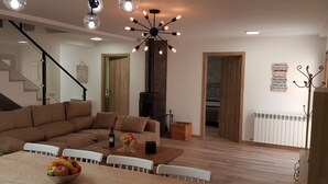 Un saló modern amb un sofà modular, una taula de dinar amb fruita, una llar de foc i una escala.