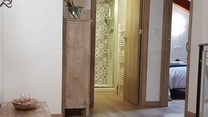 Habitació amb terra de fusta, una taula amb un bol i un got, i una porta que condueix a un bany amb cortines de dutxa estampades i un penjallatoalles.