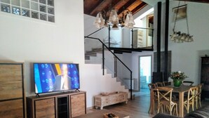 Un saló amb televisió, mobles de fusta, una escala i una zona de menjador.