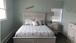 Une chambre à coucher comprenant un lit, des tables de chevet, une commode et une fenêtre avec des stores.