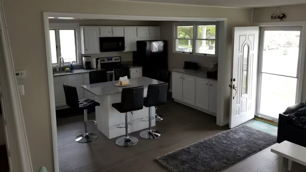 Une cuisine moderne avec des meubles blancs, un îlot central doté de tabourets, un four à micro-ondes et un réfrigérateur.