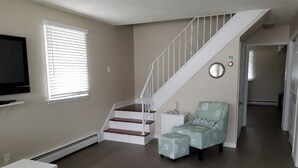 Un salon avec un escalier, un téléviseur, une petite table et une chaise.