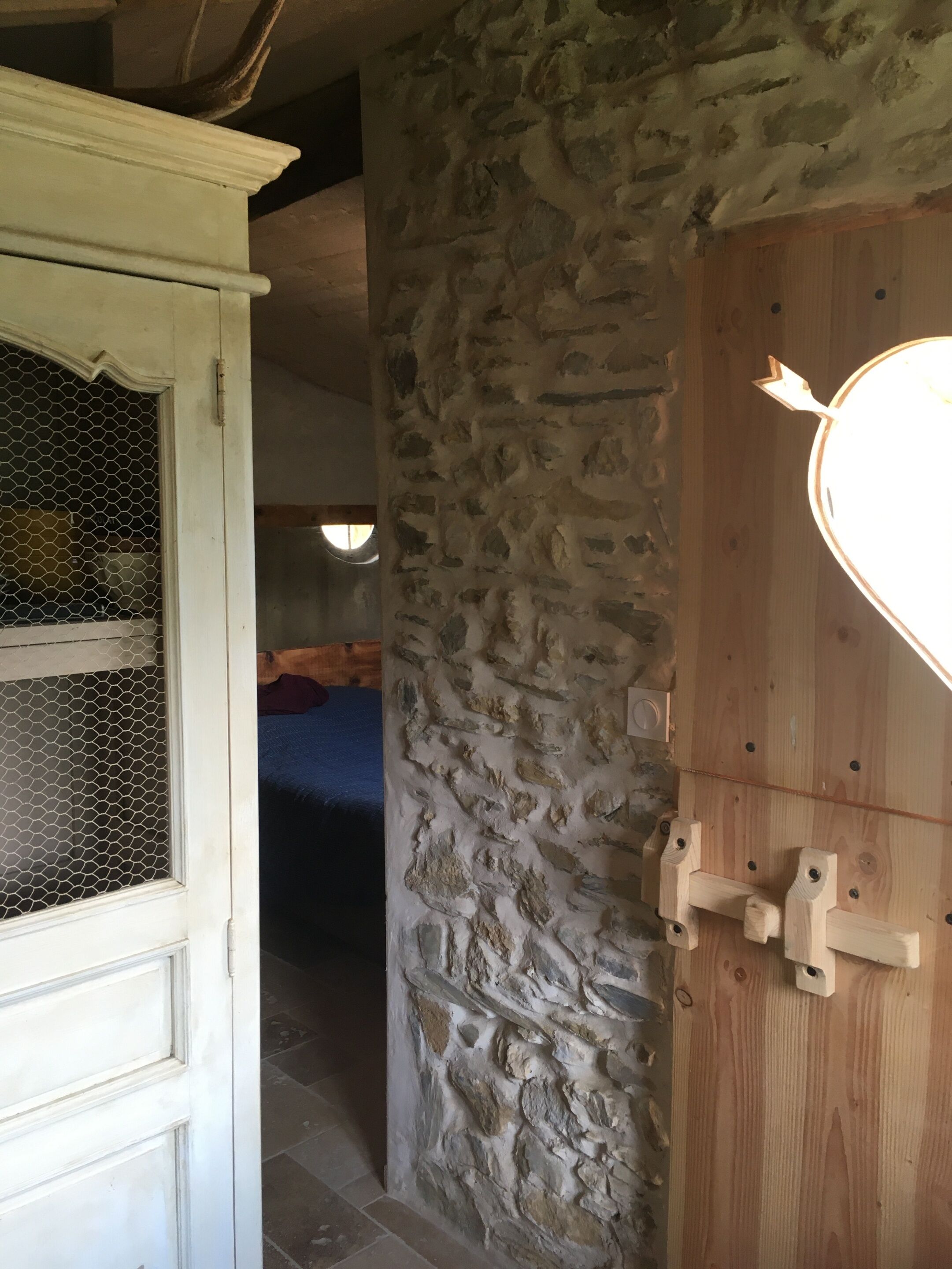 Un mur de pierre avec une porte en bois et une porte blanche munie d’un moustiquaire.