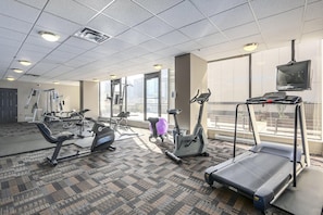 A gym with cardio machines, weight equipment, and a large window offering a city view.