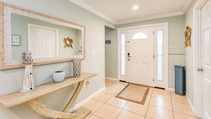 A hallway with a wooden console table, a mirror, a decorative wreath, and a sign on the wall.