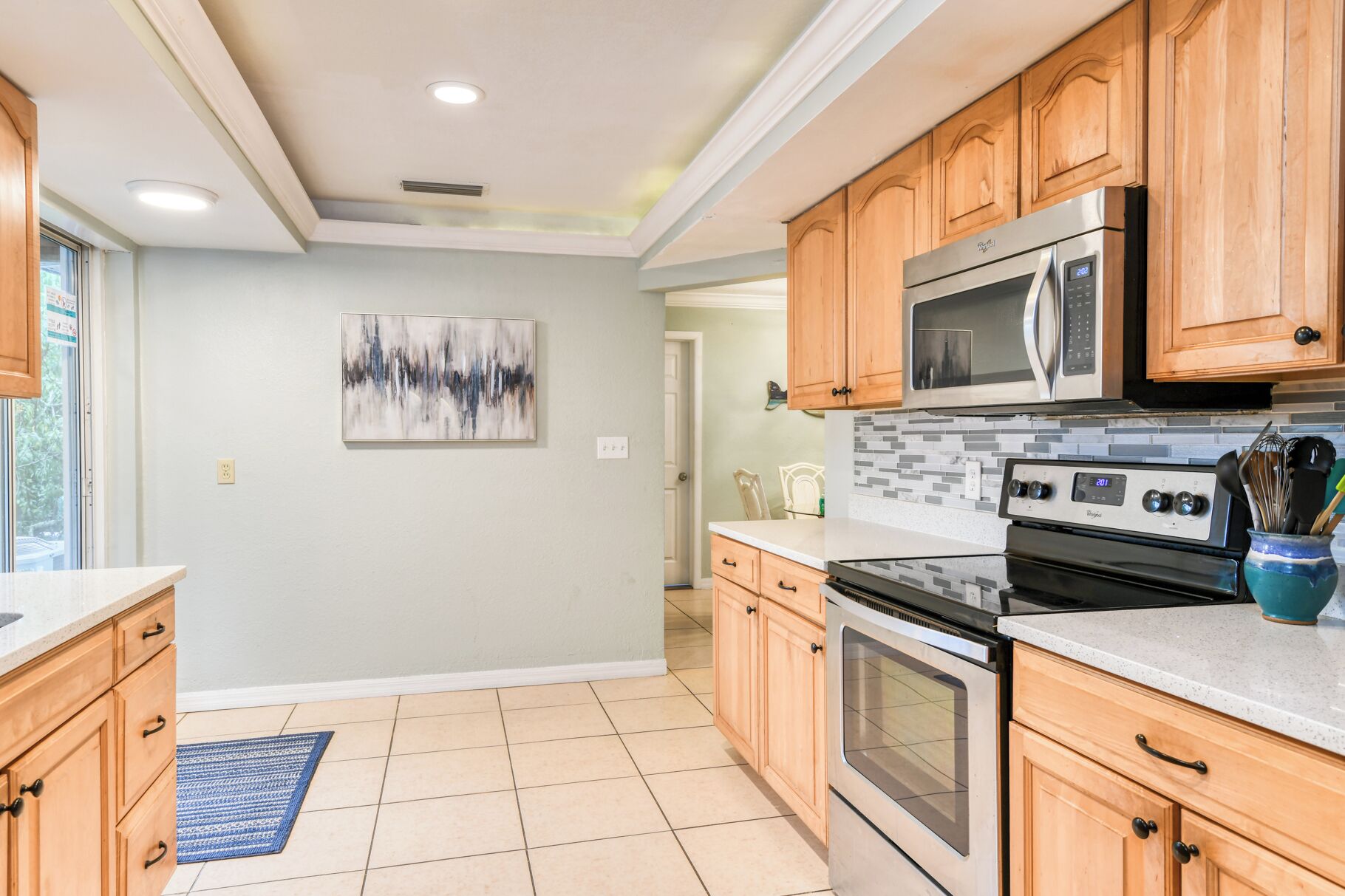 A modern kitchen with wooden cabinets, a stainless steel microwave, an oven, and a tiled floor.