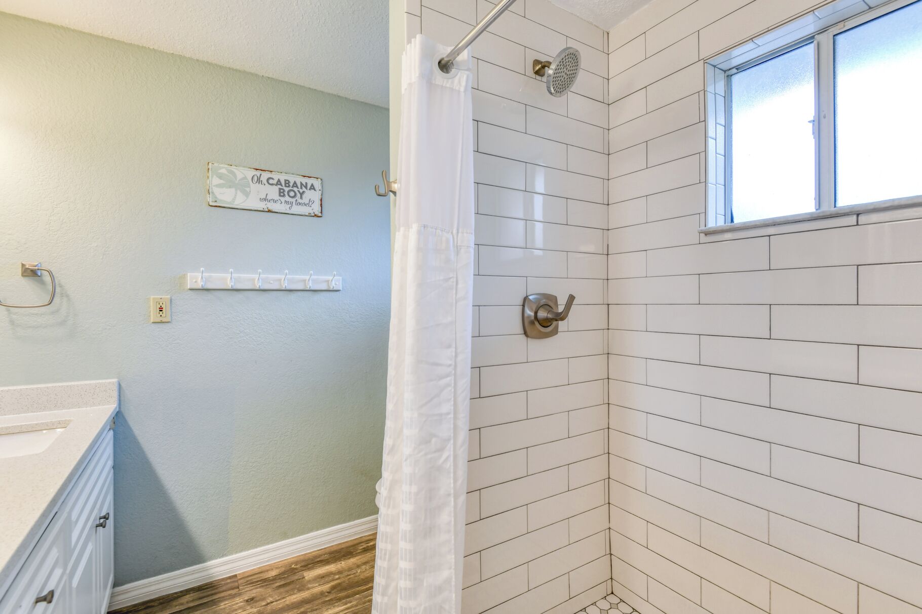 A bathroom with white subway tiles, a shower with a glass door, a towel rack, and a sign on the wall.