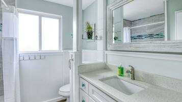 Une salle de bain comprenant des toilettes, un lavabo avec un miroir au-dessus, et une fenêtre avec un rideau.
