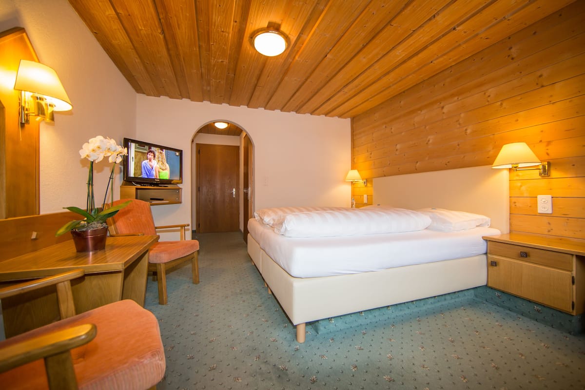 Una habitación con cama, escritorio, silla, televisión y lámpara.