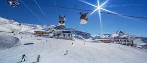 Une station de ski dotée d'un télésiège, d'un bâtiment abritant un téléski et offrant une vue sur une montagne enneigée.