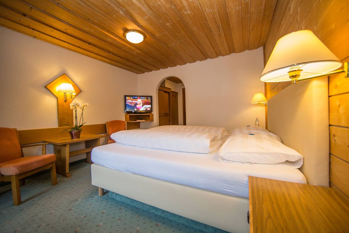 Una habitación de hotel con cama, escritorio, silla, televisor y lámpara.