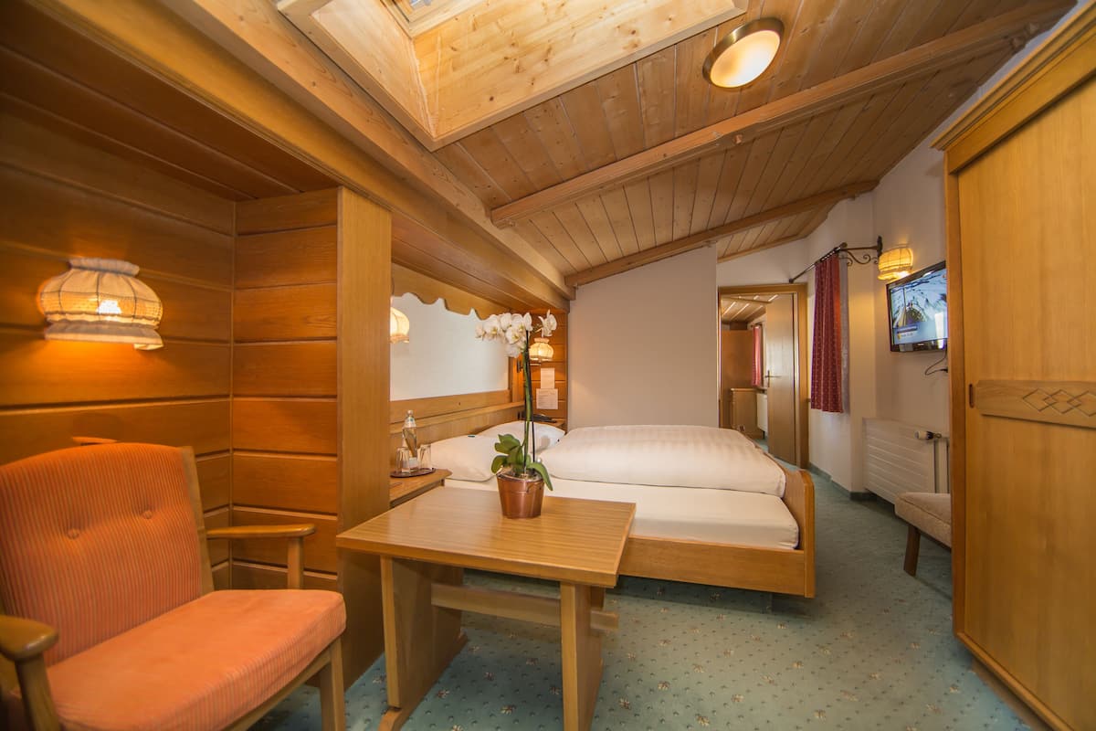 Una habitación de cabaña de madera con una cama, una mesa con una planta en maceta, una silla y una lámpara de mesa pequeña.