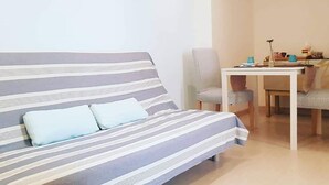 A modern room with a striped sofa, a dining table with chairs, and two wooden paddles on the wall. - Stella Marina - Stella Studio (Polignano a Mare)