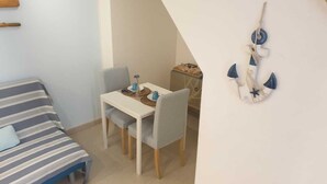 A small, cozy room with a striped sofa, a dining table with two chairs, and a wall-mounted decoration. - Stella Marina - Stella Studio (Polignano a Mare)
