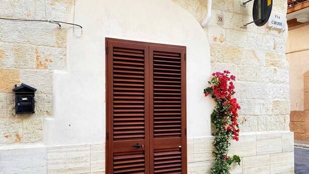 A double wooden door with horizontal slats, a mailbox, and a potted plant with red flowers against a stone wall. - Stella Marina - Stella Studio (Polignano a Mare)