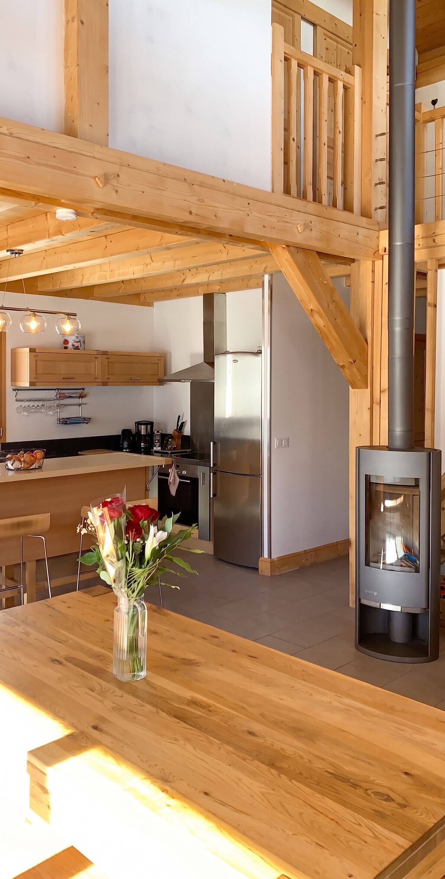 A modern kitchen with wooden beams, a central island, and a wood-burning stove.