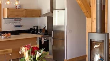 A modern kitchen with wooden beams, a central island, and a wood-burning stove.