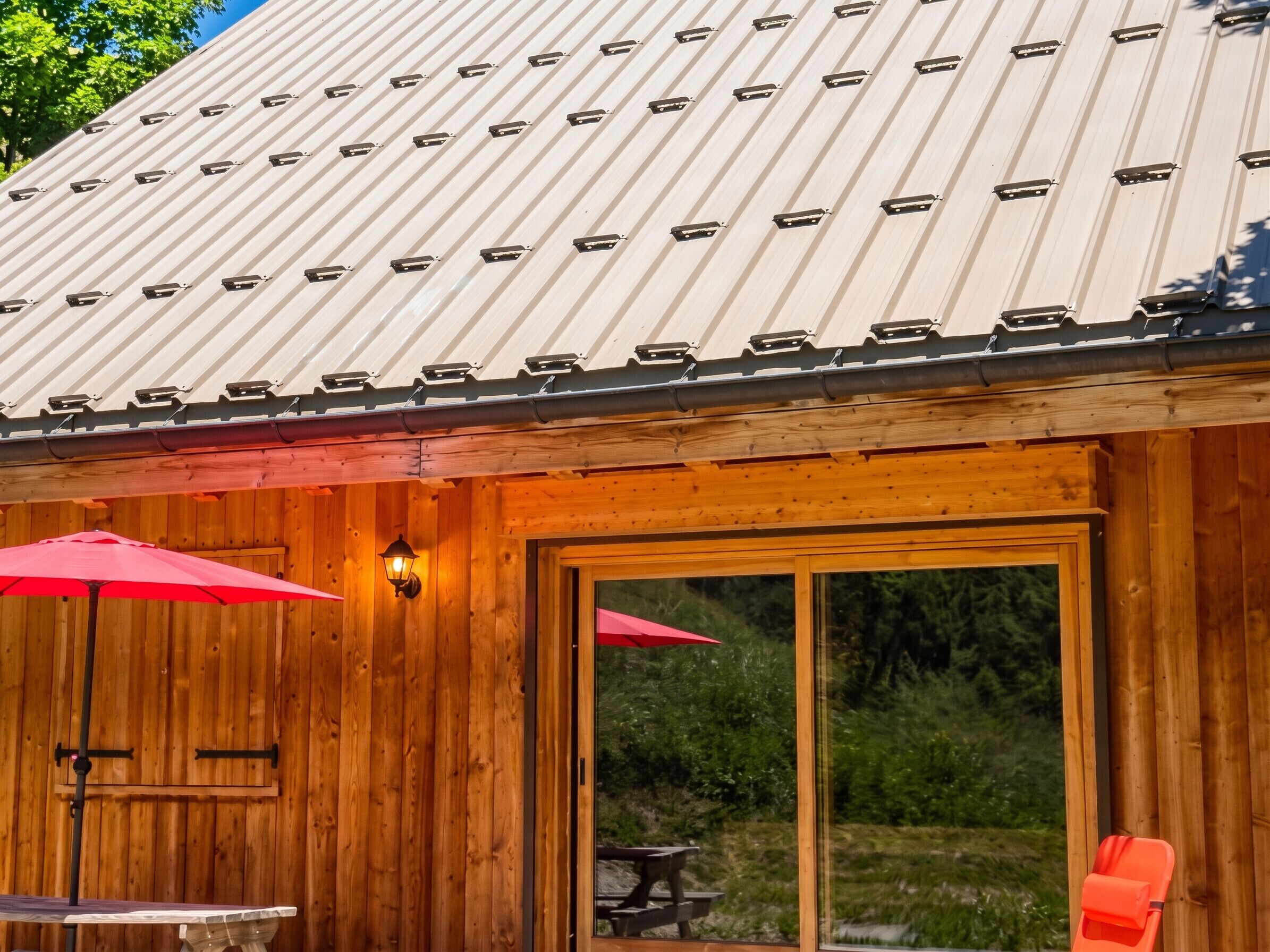 Eine Holzhütte mit einem Metalldach, einem roten Schirm und einem Holztisch.