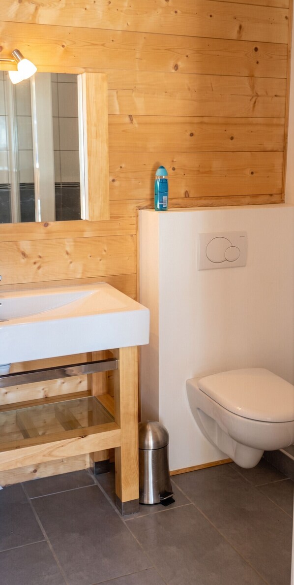 Un baño con pared de madera, un lavamanos blanco, un inodoro y un cubo de basura.