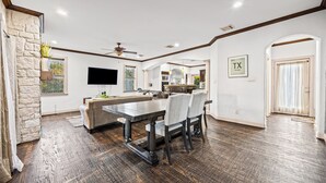 A spacious living area with a large dining table, comfortable seating, a kitchen in the background, and a stone accent wall.