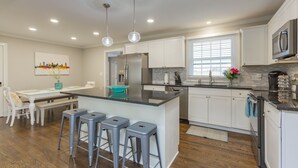 A modern kitchen with white cabinets, a central island with bar stools, stainless steel appliances, and pendant lighting.