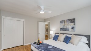A bedroom with a bed, a ceiling fan, a painting on the wall, and a door leading to a closet.