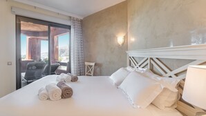 Habitación de hotel con una cama grande, vistas a través de un ventanal y una pequeña mesa con una silla.