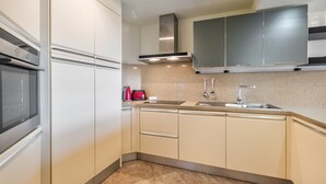 Une cuisine moderne avec des meubles blancs, une hotte de cuisinière en acier inoxydable, un évier à deux bacs et une bouilloire rouge.