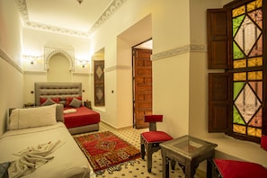 A bedroom with a bed, a red sofa, a small table, and a window with stained glass.