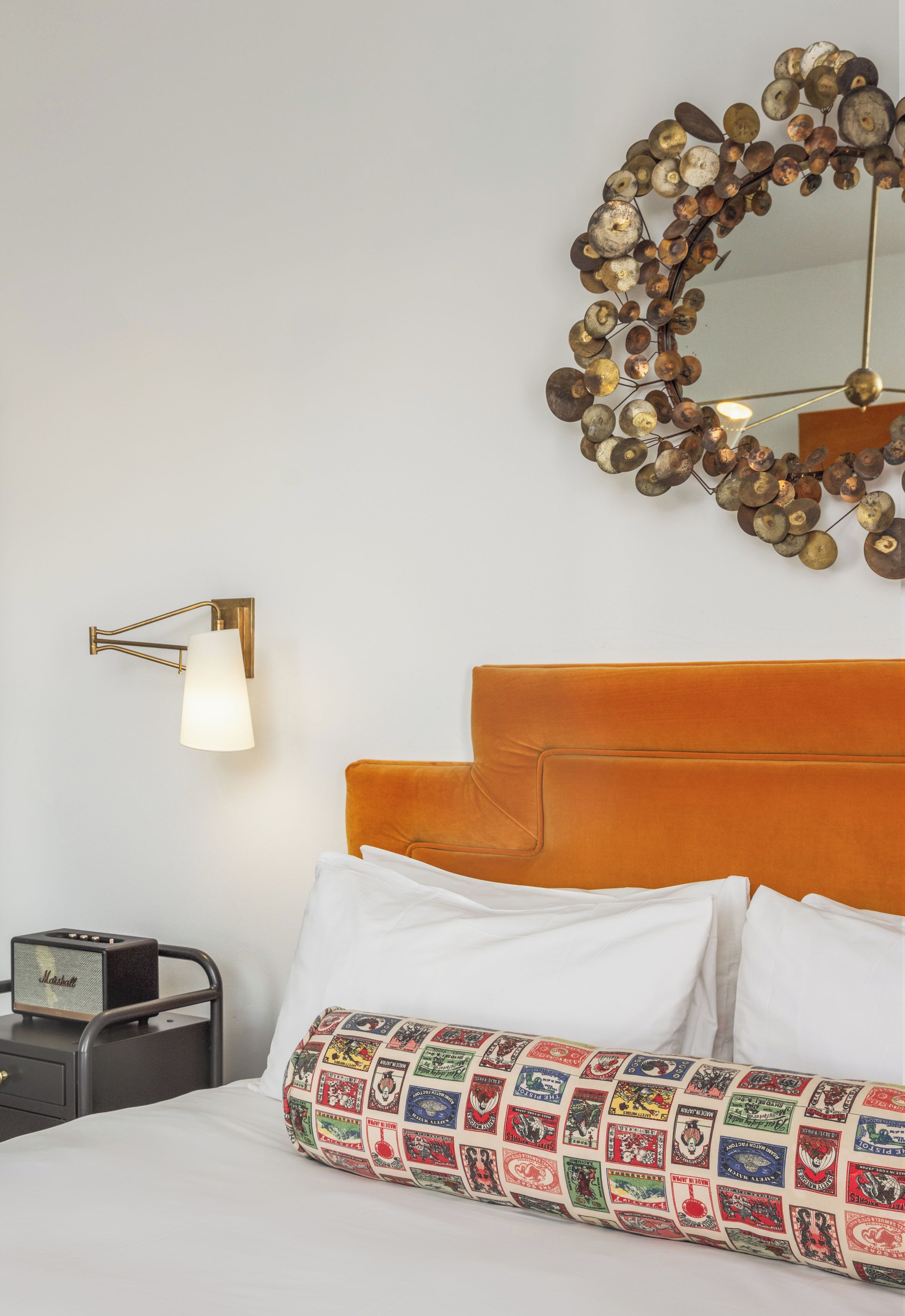 Una habitación de hotel con una cama, un espejo decorativo, una lámpara de pared y una radio antigua.