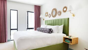 A neatly made bed with a green headboard, a bedside table with books, and decorative wall mirrors.