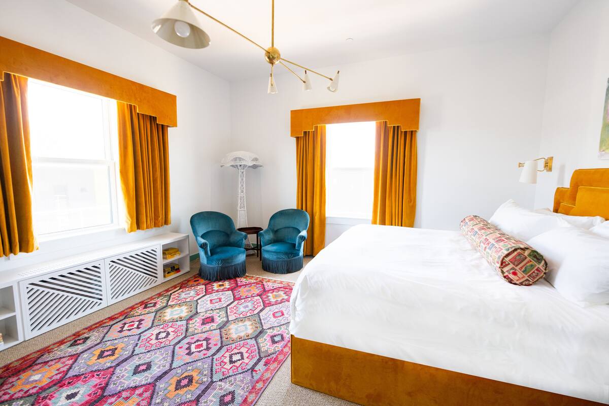Ett hotellrum med en stor säng, två fåtöljer, ett litet bord och en mönstrad matta.