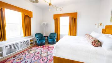 A hotel room with a large bed, two armchairs, a small table, and a patterned rug.