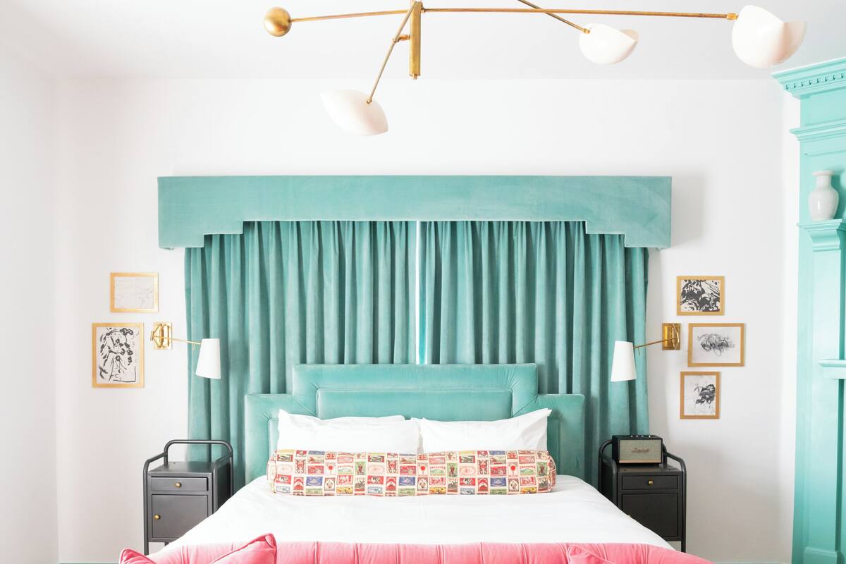 Ett sovrum med en knäppt rosa soffa, en turkos sänggavel och en modern kristallkrona.