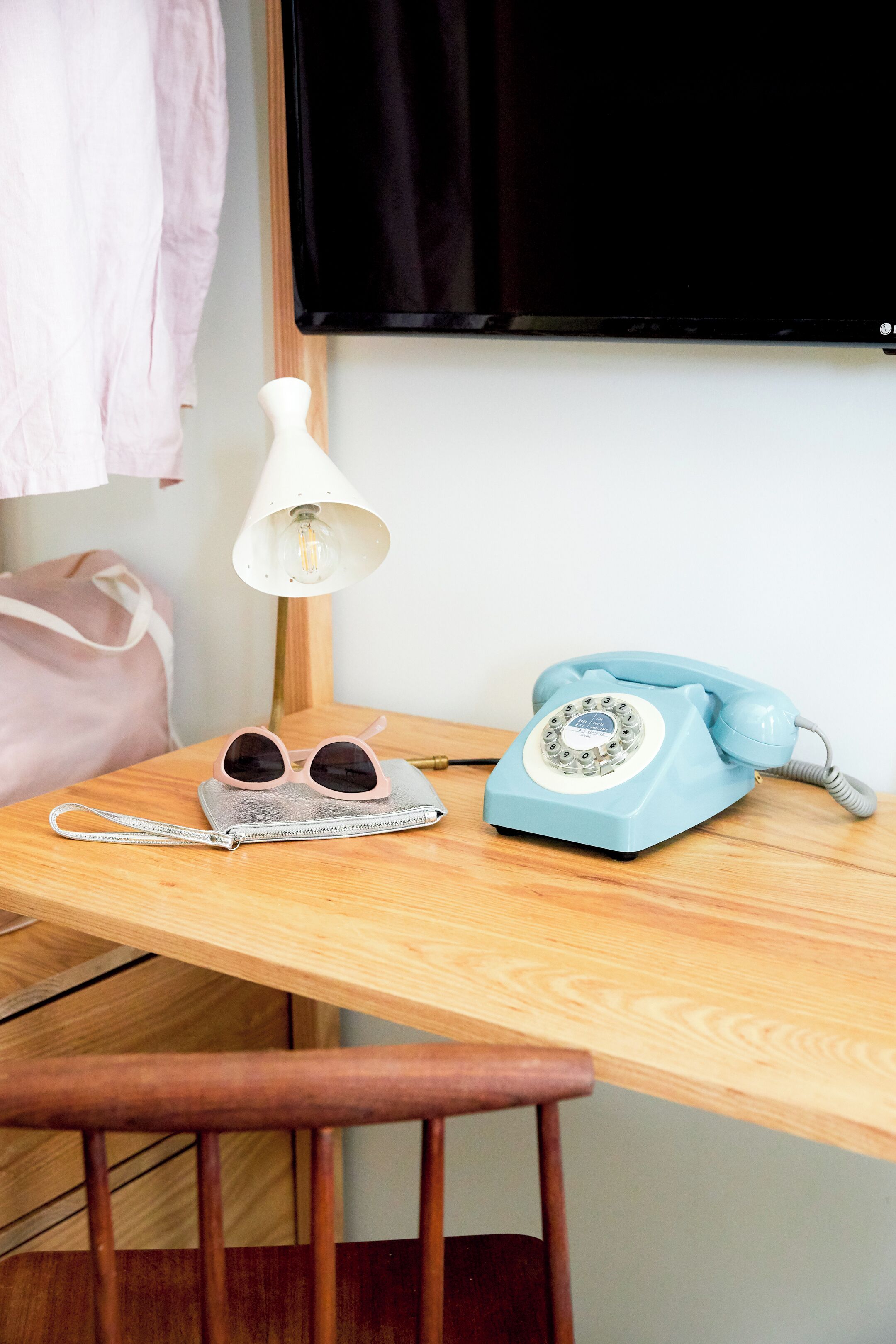 A wooden table with a vintage blue telephone, a pair of sunglasses, a lamp, and a small bag.
