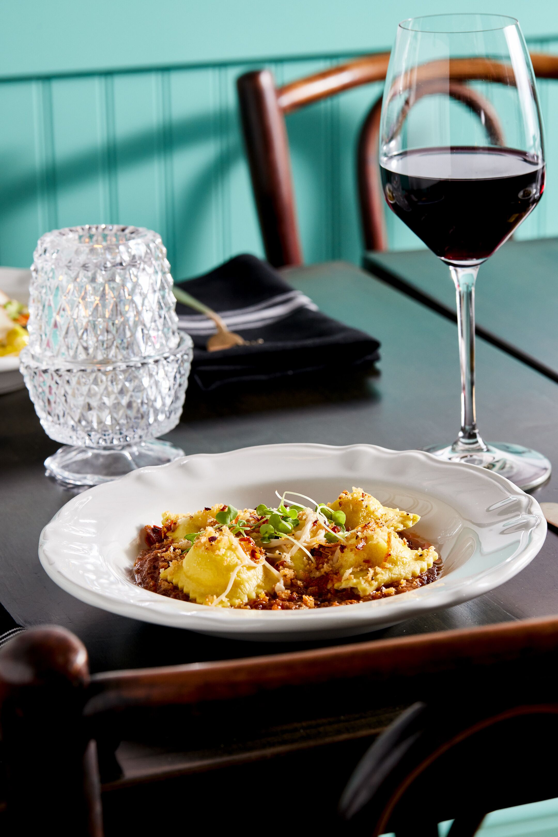 A dining table with a plate of food, a glass of red wine, and a crystal glass.