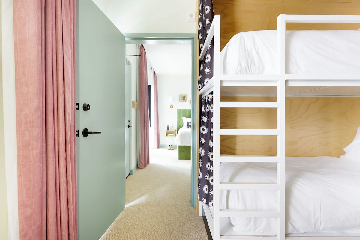 Ett hotellrum med en våningssäng, en dörr med rosa gardiner och en hall som leder till ett annat rum.