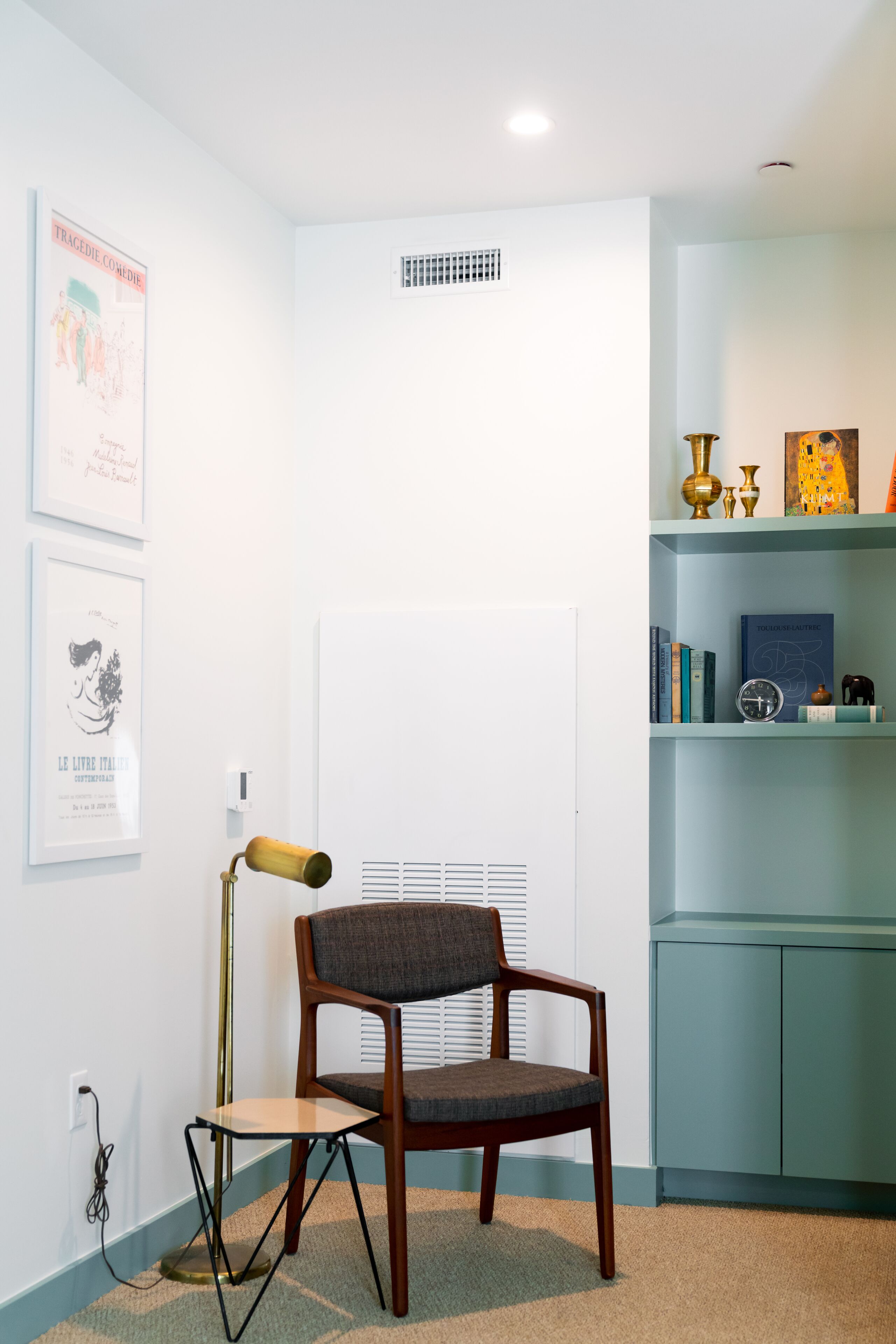 A room with a wooden chair, a desk, a bookshelf, and framed pictures on the wall.