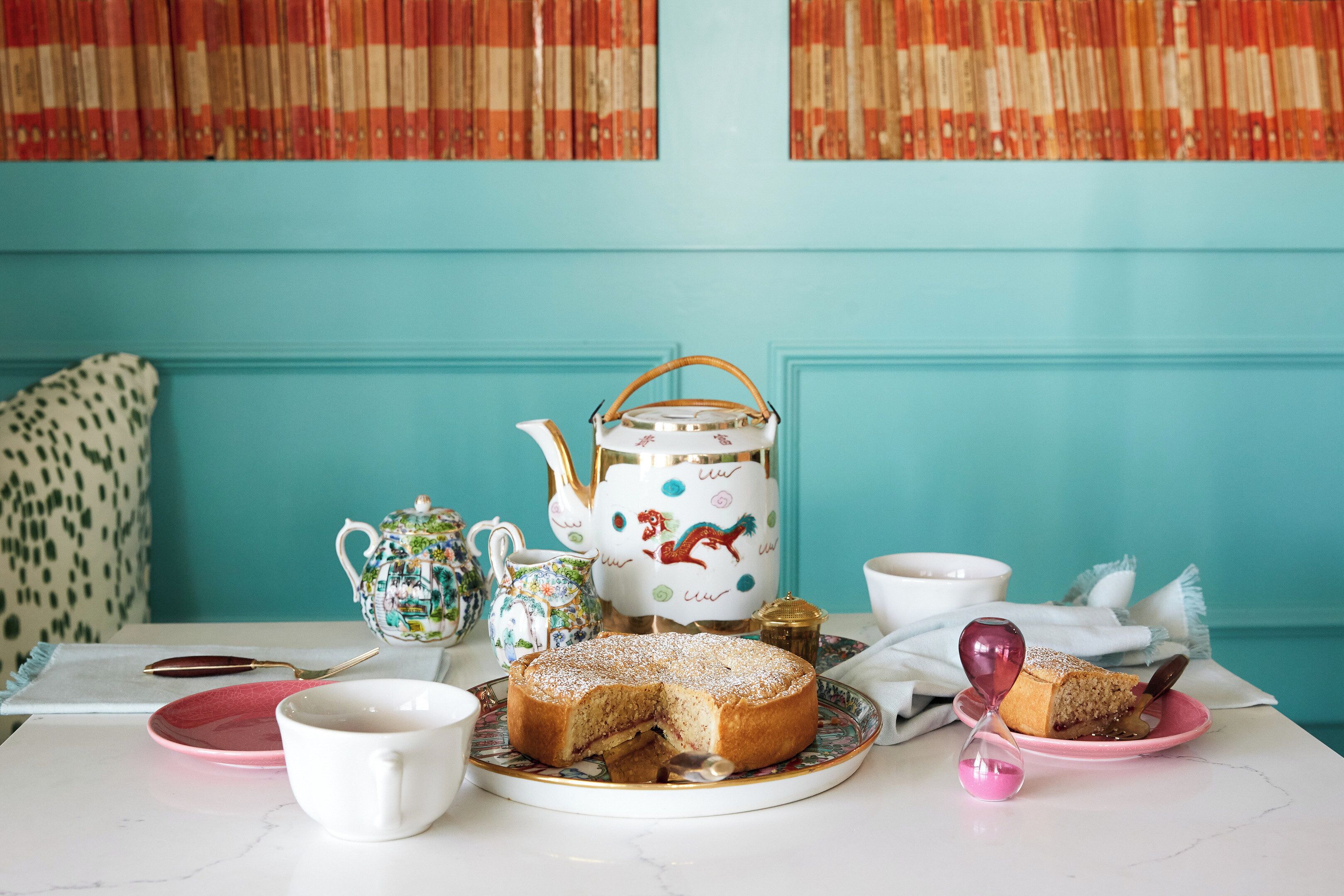 Une table dressée avec un gâteau, une théière, des tasses et un sablier décoratif.