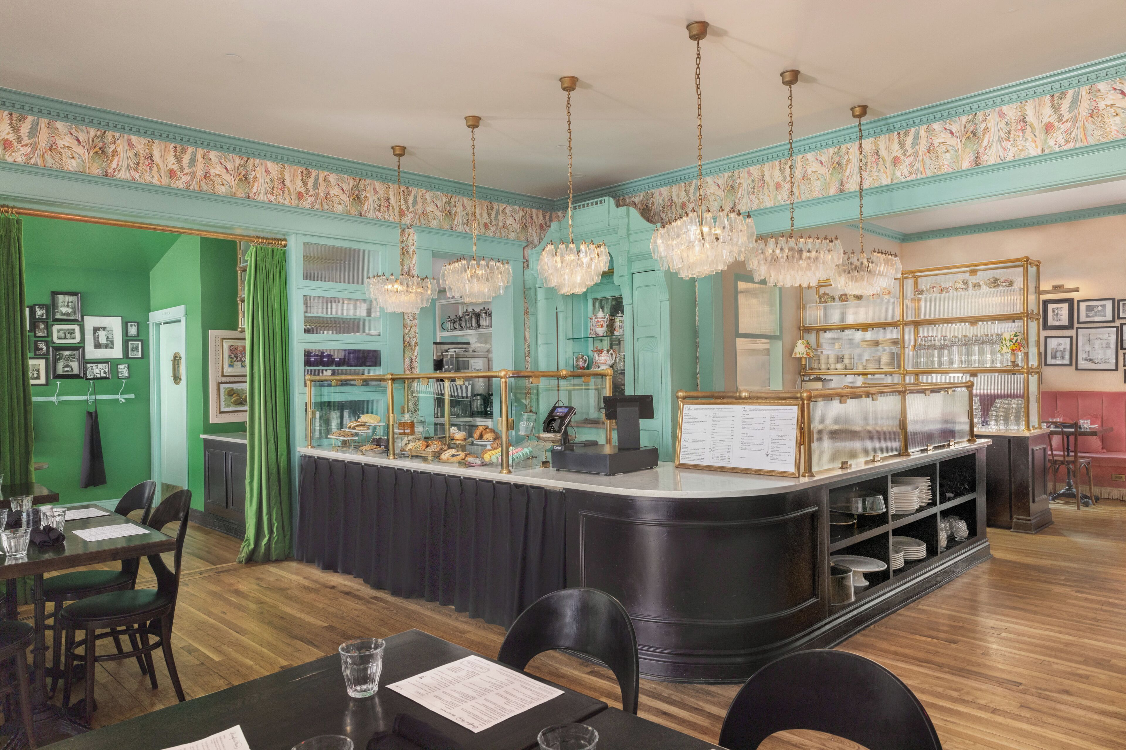 A restaurant with a teal-colored wall, a counter with a display case, and hanging crystal chandeliers.