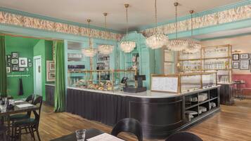 A restaurant with a teal-colored wall, a counter with a display case, and hanging crystal chandeliers.