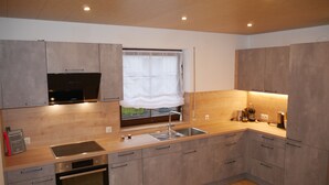 A modern kitchen with grey cabinets, a built-in oven, a stainless steel sink, and a window with a white curtain. - Geiger's apartment in the Laucherttal (Veringenstadt)
