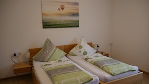 A double bed with green and white bedding, two nightstands, a wall-mounted lamp, and a painting of hot air balloons. - Geiger's apartment in the Laucherttal (Veringenstadt)
