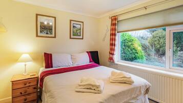 A bedroom with a bed, a nightstand, a lamp, two framed pictures on the wall, and a window with curtains.