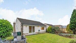 Een gelijkvloers huis met schuin dak, een veranda en een kleine tuin met gazon en enkele struiken.