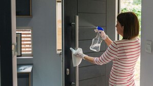 Une personne nettoie une poignée de porte à l’aide d’un vaporisateur et d’un chiffon.