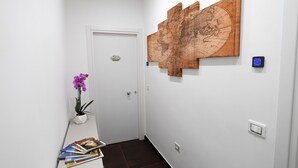 A hallway with a white door, a wall-mounted map, a potted orchid, and a stack of magazines. - B&B In Centro Storico Salerno (Salerno)