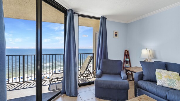A balcony with a view of the beach and ocean, a sofa, a chair, and a small table.