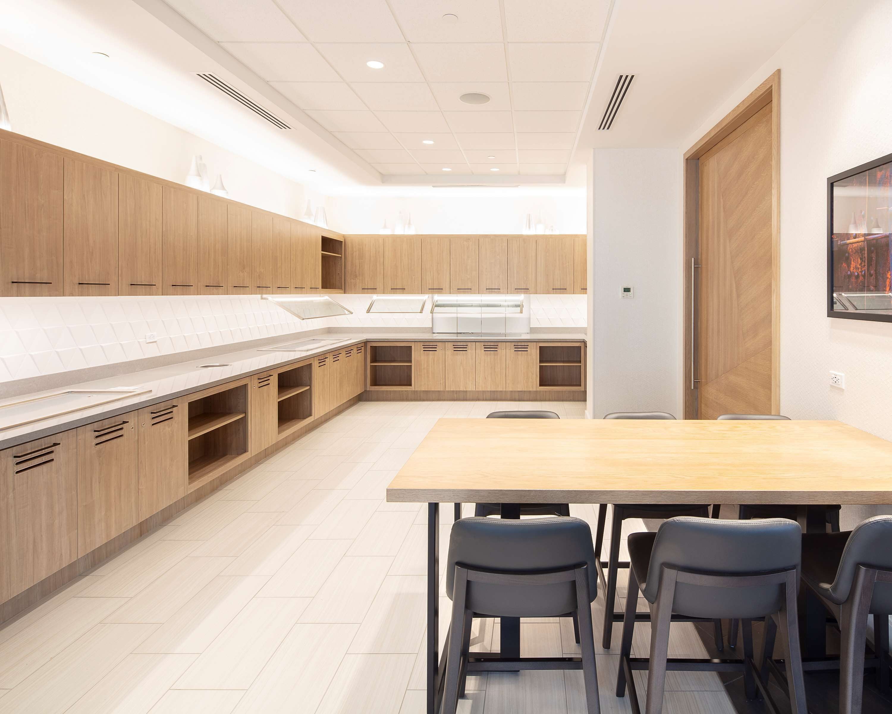A modern kitchen with wooden cabinets, a large island, and a dining area with four chairs.